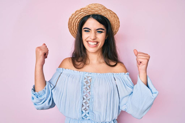 Brunette teenager girl wearing summer hat screaming proud, celebrating victory and success very excited with raised arms  - Photo, image