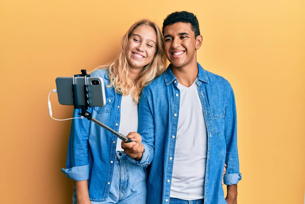 Νεαρό διαφυλετικό ζευγάρι παίρνει μια φωτογραφία selfie με smartphone χαμογελώντας με ένα χαρούμενο και δροσερό χαμόγελο στο πρόσωπο. που δείχνει δόντια.  - Φωτογραφία, εικόνα