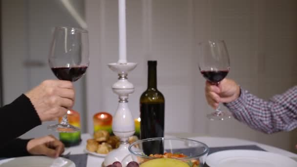Primer plano de copas de vino tinto tintineo durante la cena romántica. Feliz alegre pareja de ancianos mayores - Metraje, vídeo