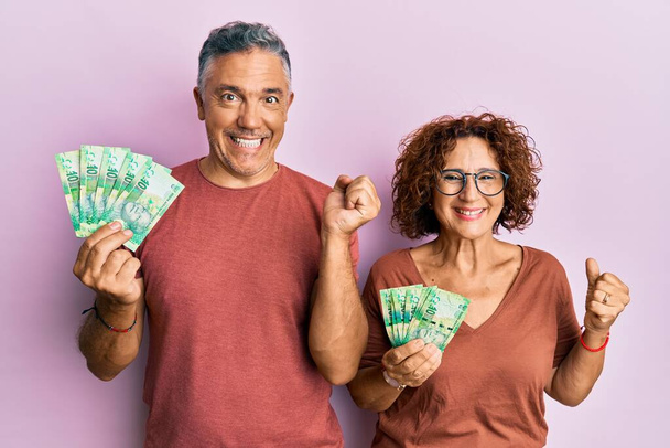 Красива пара середнього віку тримає південноафриканські банкноти 10 рандових, що кричать гордо, святкуючи перемогу і успіх дуже схвильовані піднятою рукою
  - Фото, зображення