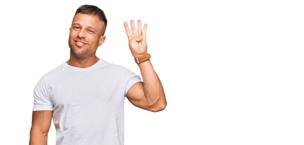 Όμορφος άνθρωπος των μυών φορώντας casual λευκό μπλουζάκι δείχνει και δείχνει προς τα πάνω με τα δάχτυλα νούμερο τέσσερα, ενώ χαμογελά αυτοπεποίθηση και χαρούμενος.  - Φωτογραφία, εικόνα