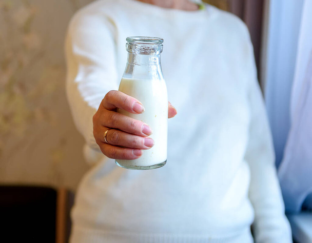 Egy fehér pulóveres nő friss tejet tart a kezében.. - Fotó, kép