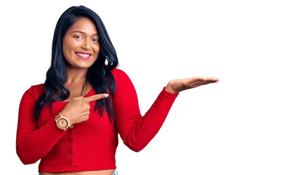 Mulher hispânica com cabelos longos vestindo roupas casuais espantado e sorrindo para a câmera enquanto se apresenta com a mão e apontando com o dedo.  - Foto, Imagem