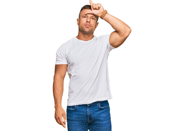 Handsome muscle man wearing casual white tshirt making fun of people with fingers on forehead doing loser gesture mocking and insulting.  - Fotoğraf, Görsel