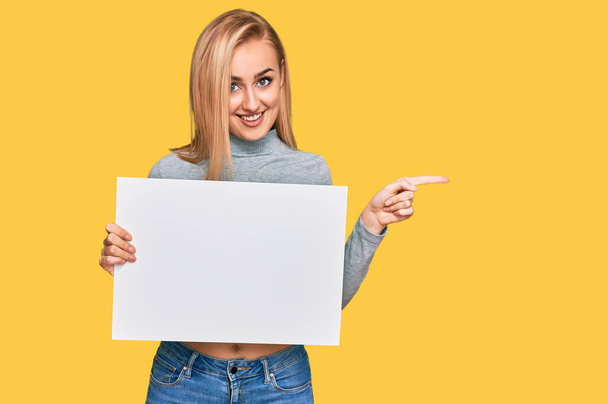 Beautiful caucasian woman holding blank empty banner smiling happy pointing with hand and finger to the side  - Photo, Image