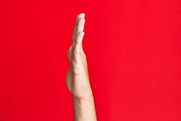 Arm of caucasian white young man over red isolated background showing side of stretched hand, pushing and doing stop gesture  - Photo, Image