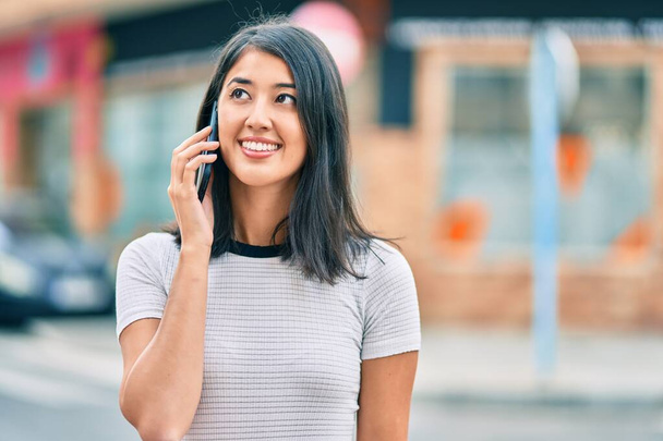 Fiatal spanyol nő mosolyog boldog beszél az okostelefonon a városban. - Fotó, kép