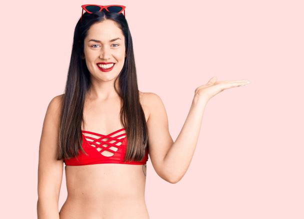 Young beautiful caucasian woman wearing bikini smiling cheerful presenting and pointing with palm of hand looking at the camera.  - Photo, Image