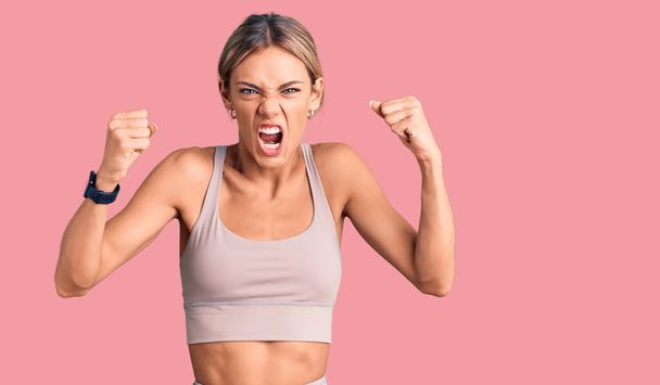 Beautiful caucasian woman wearing sportswear angry and mad raising fists frustrated and furious while shouting with anger. rage and aggressive concept.  - Foto, imagen
