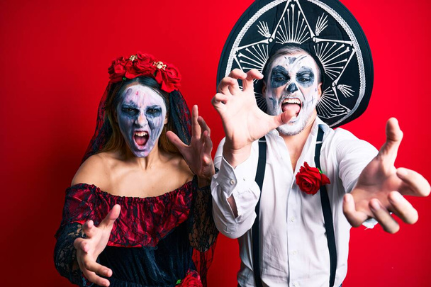 Beautiful couple wearing day of the dead costume gesturing as a zombie over isolated red background. - Fotoğraf, Görsel