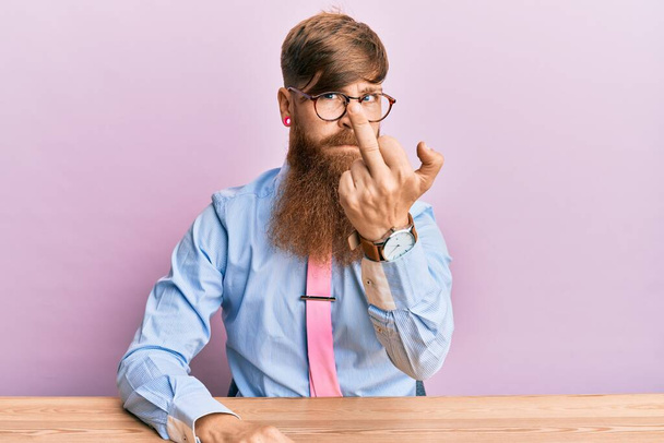Young irish redhead man wearing business shirt and tie sitting on the table showing middle finger, impolite and rude fuck off expression  - Fotografie, Obrázek