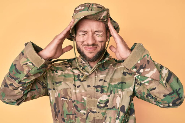 Nuori valkoihoinen mies naamioituneena armeijan univormuun käsi pään päällä, päänsärky stressin takia. migreeni.  - Valokuva, kuva