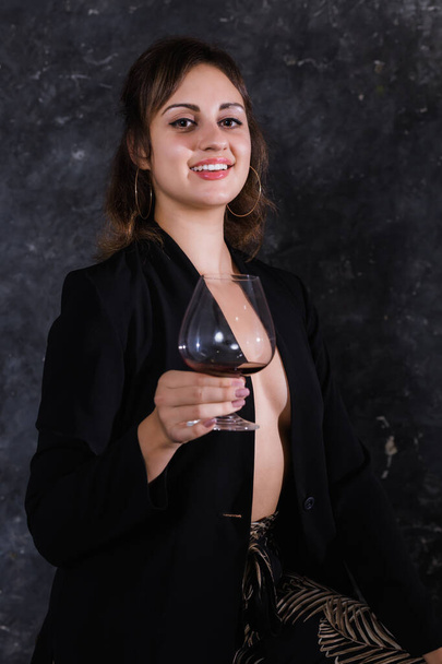 Siyah ceketli güzel bir bayan ve bir kadeh şarap. - Fotoğraf, Görsel