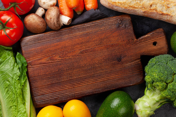 Varias verduras, frutas y pan en la mesa de piedra y tabla de cortar vacía. Vista superior plano con espacio de copia - Foto, Imagen