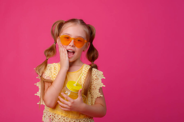 una bambina in occhiali da sole con un cocktail su sfondo rosa  - Foto, immagini