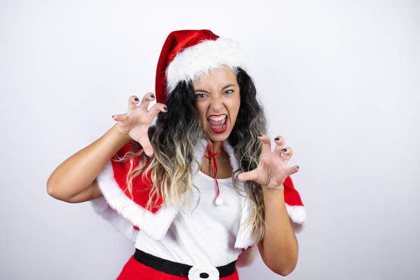 Young beautiful woman wearing a Santa Claus costume over white background smiling funny doing claw gesture as cat, aggressive and sexy expression - Φωτογραφία, εικόνα