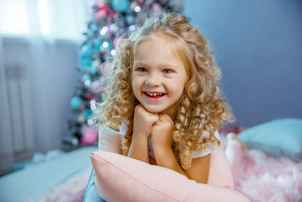 una bambina vicino all'albero di Natale è sdraiata sul letto   - Foto, immagini