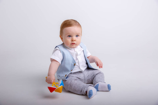 cute baby boy sitting with toy on floor in studio against gray background - Valokuva, kuva