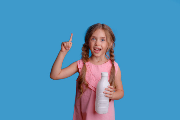 dziewczynka trzyma butelkę mleka na niebieskim tle - Zdjęcie, obraz