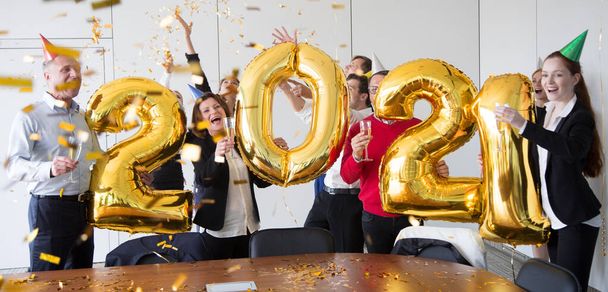 La gente de negocios está celebrando las vacaciones en la oficina moderna bebiendo champán y divirtiéndose en el coworking. Feliz Navidad y Feliz Año Nuevo 2021. Números de globos - Foto, imagen
