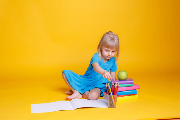 Concept of preschool education, girl with stack of books and apple against orange background - Photo, Image