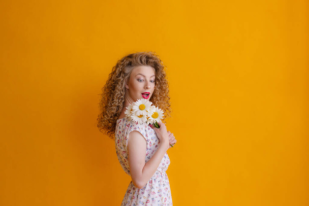 una joven con el pelo rizado sosteniendo un ramo de margaritas sobre un fondo naranja   - Foto, imagen