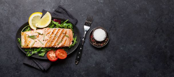 Filetto di pesce salmone alla griglia con sale, pepe e rosmarino sopra le foglie di insalata. Sul tavolo di pietra. Vista dall'alto posa piatta con spazio di copia - Foto, immagini