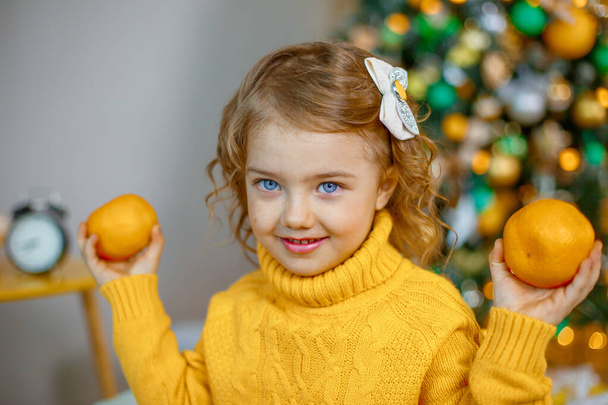 little girl playing with tangerines near the Christmas tree  - Φωτογραφία, εικόνα