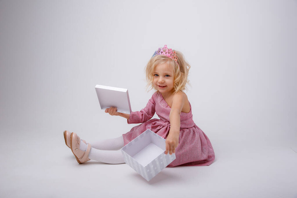 une petite fille avec un cadeau s'assoit sur un fond gris - Photo, image