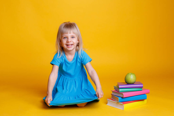 Concept of preschool education, girl with stack of books and apple against orange background - Photo, Image