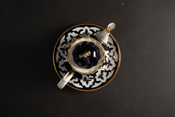 Etnické uzbecké keramické nádobí na černém pozadí. Dekorativní keramický podšálek a konvice s tradičním ornamentem. - Fotografie, Obrázek