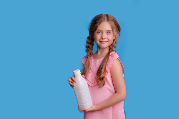 kislány kezében egy üveg tej a kék háttér - Fotó, kép
