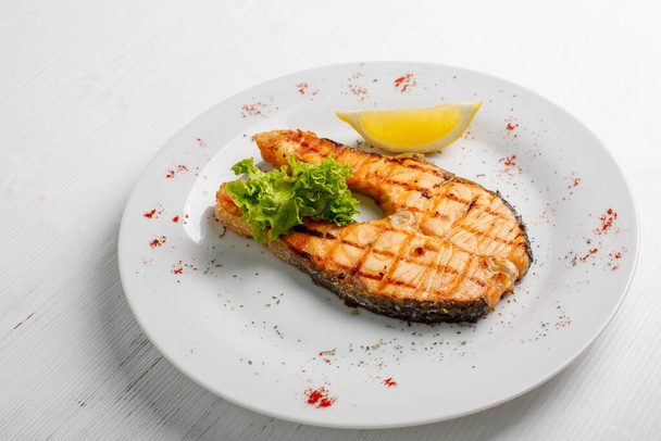 grilled salmon with lemon and lettuce on white plate - Фото, изображение