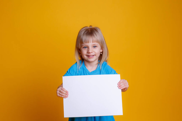Baby Mädchen mit einem leeren Blatt Papier, aufgebracht posiert auf gelbem Hintergrund  - Foto, Bild