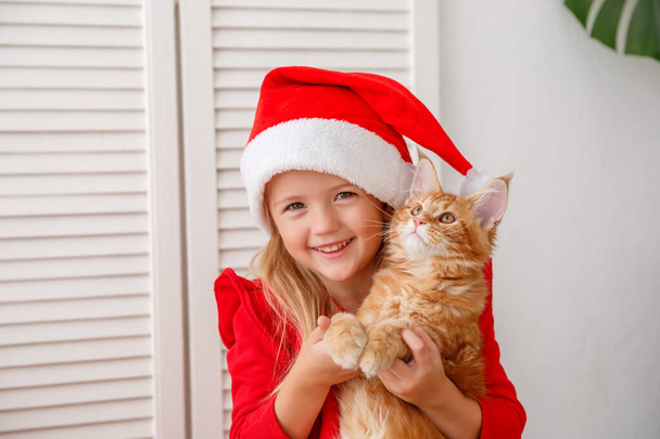 schattig klein meisje in santa hoed met kat - Foto, afbeelding