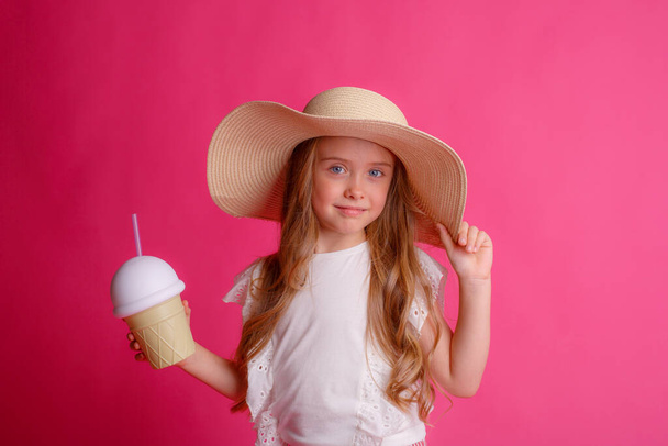 портрет маленької блондинки в капелюсі на рожевому тлі з банкою охолоджуючого коктейлю
. - Фото, зображення