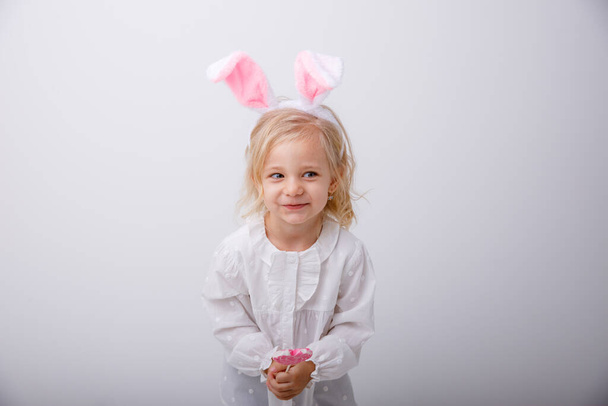Portré egy aranyos kislányról, nyúlfülekkel, fehér háttéren, nyalókával a kezében. Húsvét fogalma - Fotó, kép
