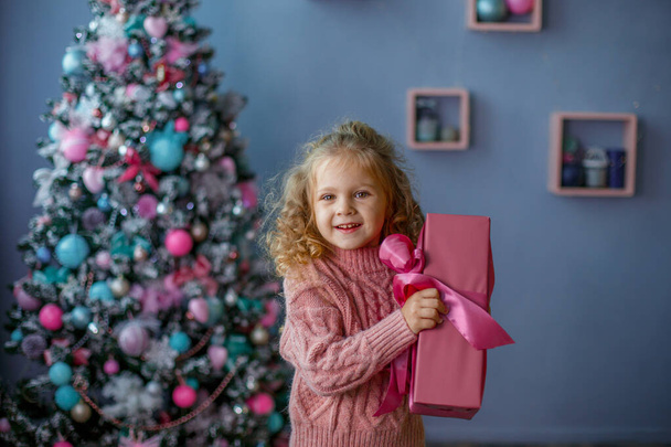 holčička v blízkosti vánočního stromečku drží dárek s úsměvem  - Fotografie, Obrázek