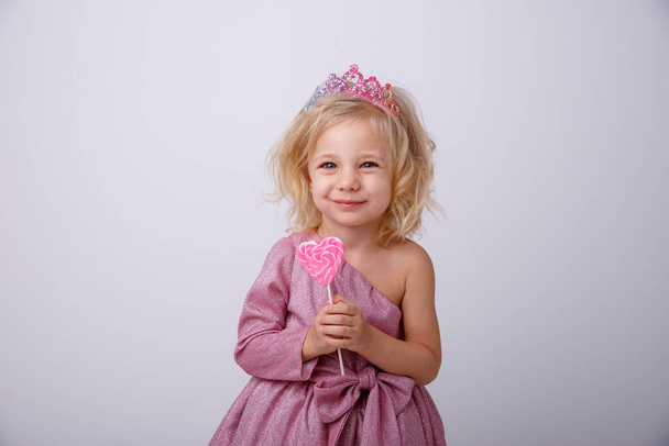 красивая маленькая блондинка позирует с леденец в форме сердца  - Фото, изображение