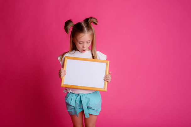 Portrait of a girl holding an empty frame, place for text, on a pink background  - Foto, immagini