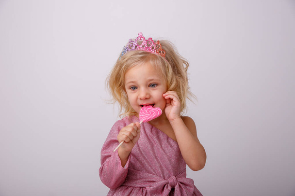 beautiful little blonde girl posing with a heart shaped Lollipop  - Fotoğraf, Görsel
