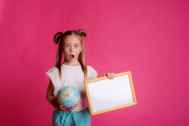 Portrait of a girl holding a globe in her hands and an empty frame on a pink background - Foto, imagen