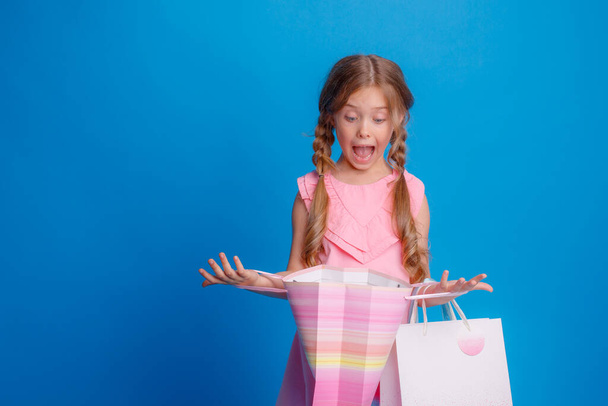 Uma menina com um monte de sacos de compras feliz em um fundo azul no estúdio  - Foto, Imagem