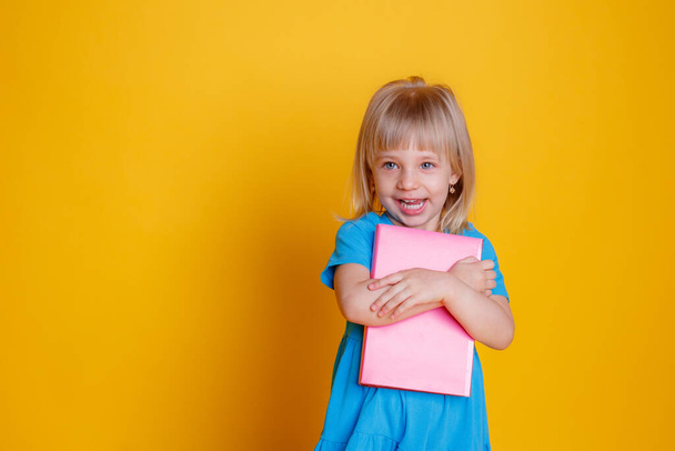 portrait of a cute little girl holding a book on orange background - Foto, Imagen