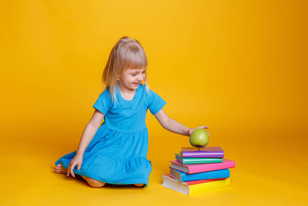 Έννοια της προσχολικής εκπαίδευσης, κορίτσι με στοίβα από βιβλία και μήλο σε πορτοκαλί φόντο - Φωτογραφία, εικόνα