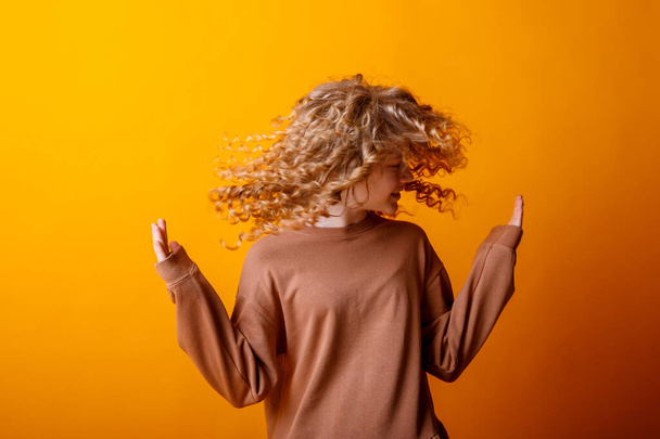 fille secouant la tête sur fond orange en studio - Photo, image