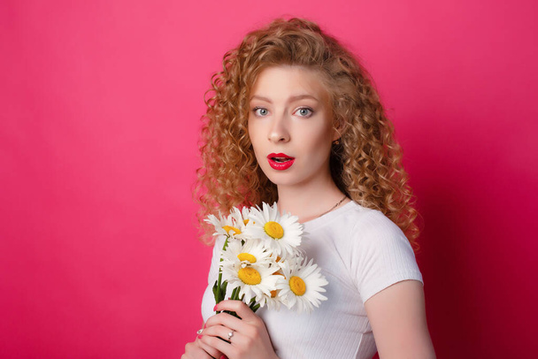 curly girl holding a bouquet of daisies on pink background  - Photo, image