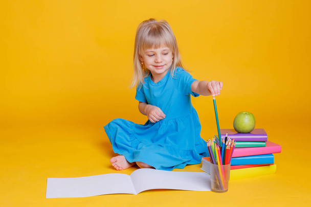 Concepto de educación preescolar, niña con pila de libros y manzana sobre fondo naranja - Foto, imagen
