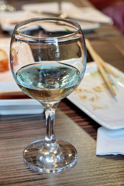 Bicchiere con avanzi di vino bianco sul fondo tavola dopo pasto, cornice verticale - Foto, immagini