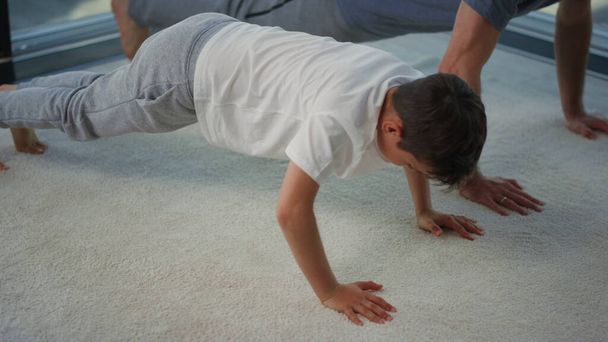 Father and son training together at home. Dad and child doing push ups indoors - Foto, immagini